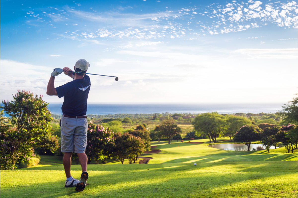 Man hitting golf ball down hill towards ocean and horizon. Photography by Allen.G. Image via Shutterstock