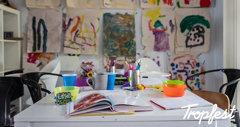 shot of a table with childrens paint and pencils with paintings in the background