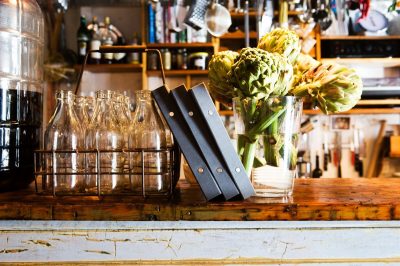 Bar top at restaurant with menus, artichoke flowers and water glasses