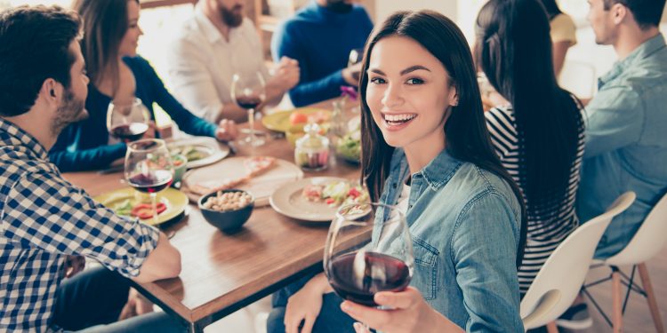 A girl holding a glass of red wine at a party with friends. Image: Roman Samborskyi