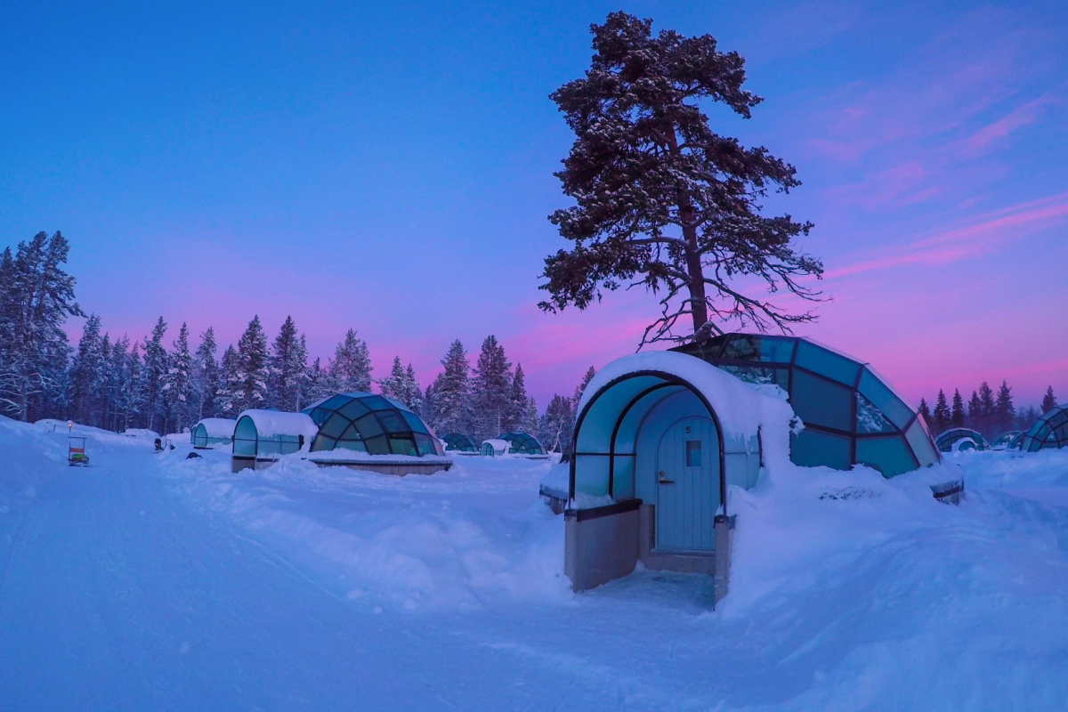 Sunrise above amazing glass igloo village at Kakslauttanen Arctic Resort Finland. Photography by Flystock. Image via Shutterstock