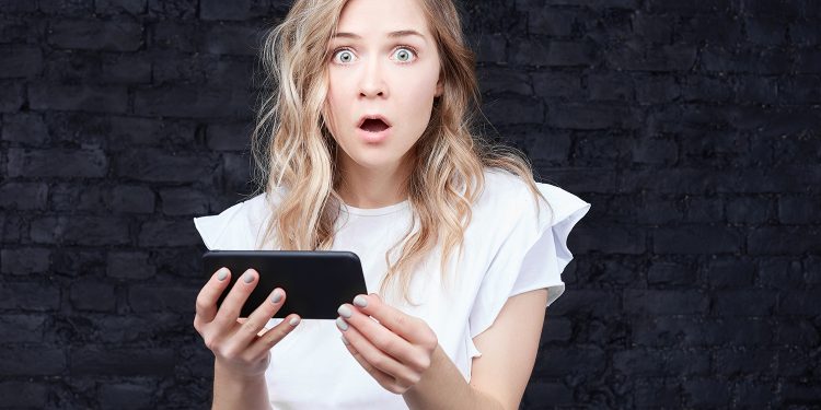 Woman shocked by something on phone. Photographed by traveliving. Image via Shutterstock