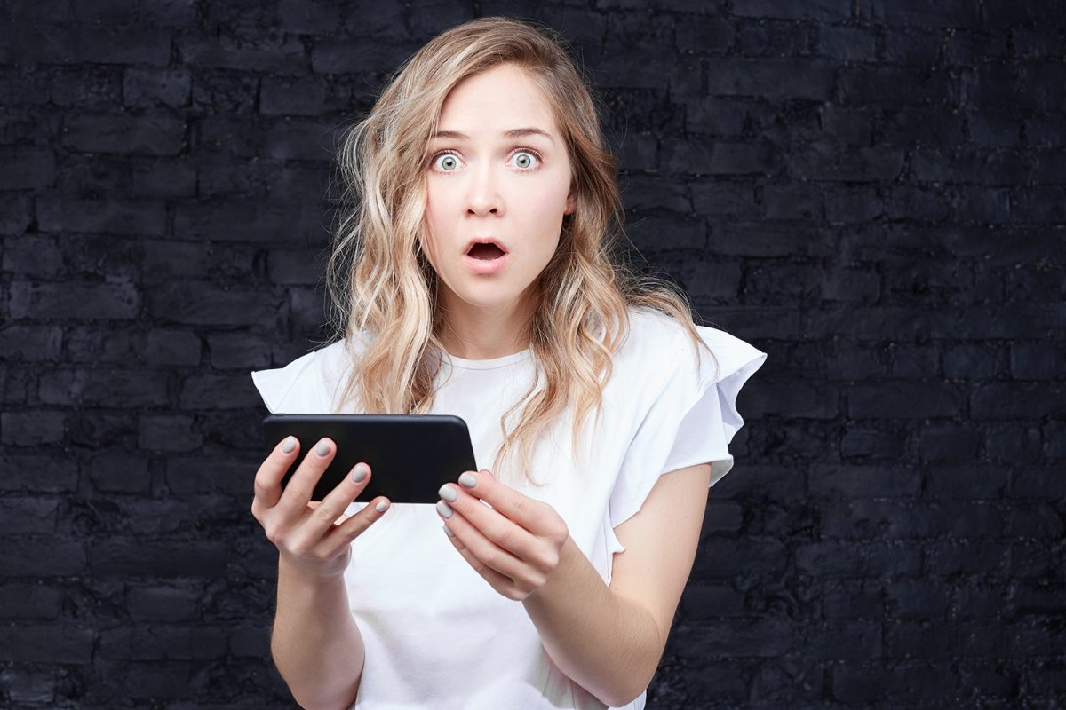 Woman shocked by something on phone. Photographed by traveliving. Image via Shutterstock