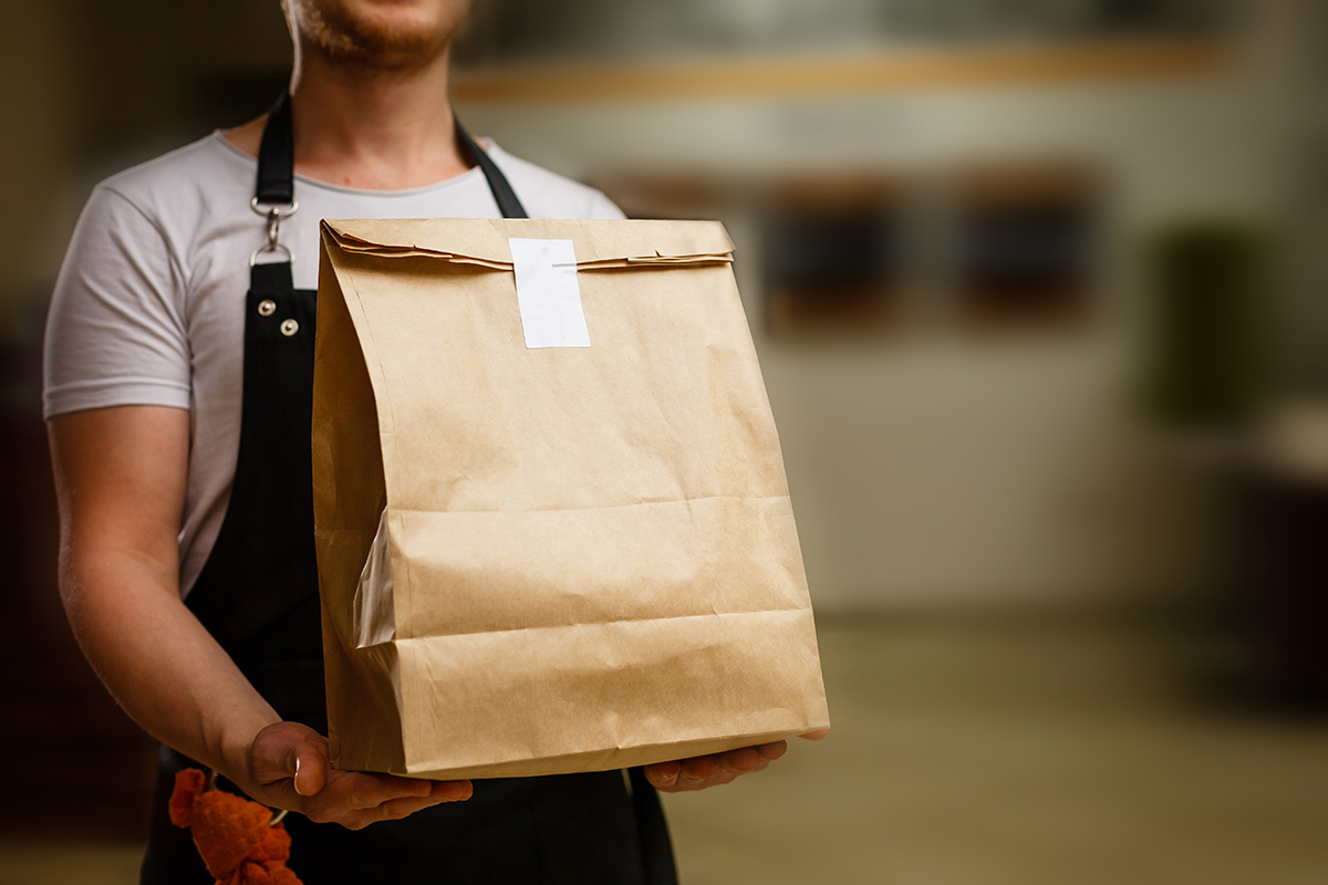 Image of waiter holding delivery bag of food. Image Via Shutterstock