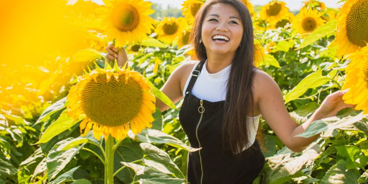Happy woman amongst sunflowers. Photographed by Courtney Cook. Sourced via Unsplash