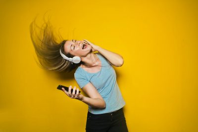 Woman singing and listening to music. Photographed by Bruce Mars. Image via Unsplash