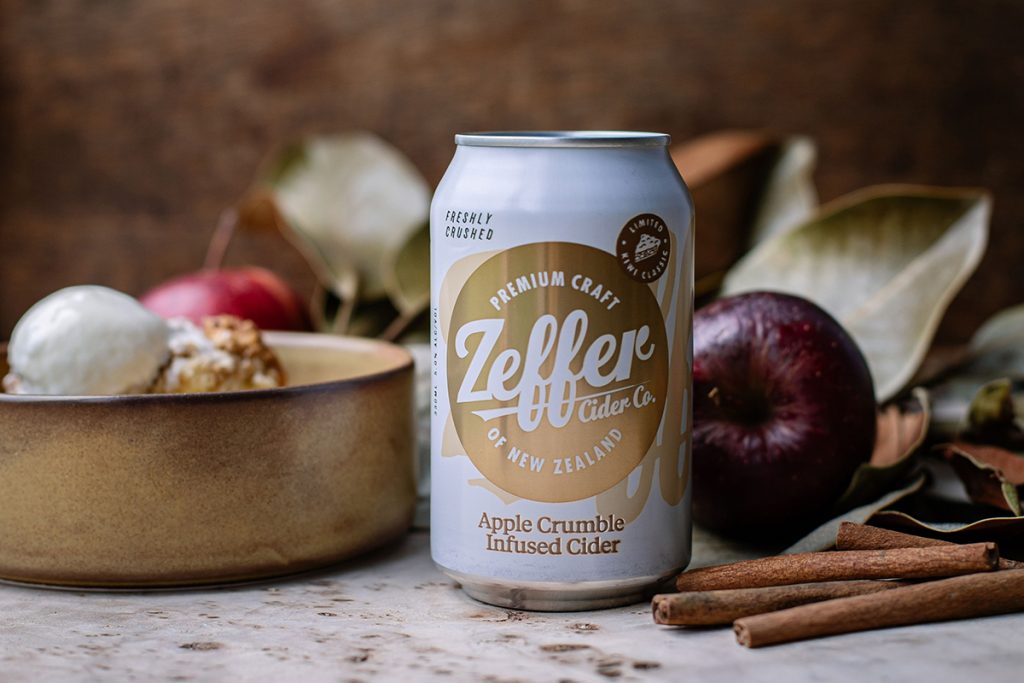 White and gold can of Zeffer Cider Co's Apple Crumble Infused Cider placed amongst fresh ingredients like apples and cinnamon. Image supplied
