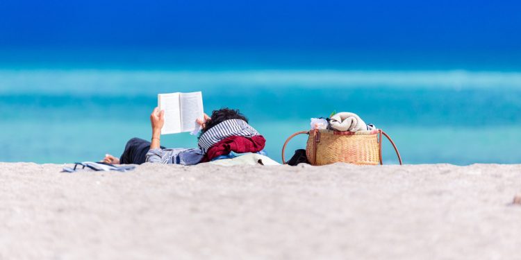 Man reading a book on the beach. Photographed by Dan Dumitriu. Sourced via Unsplash