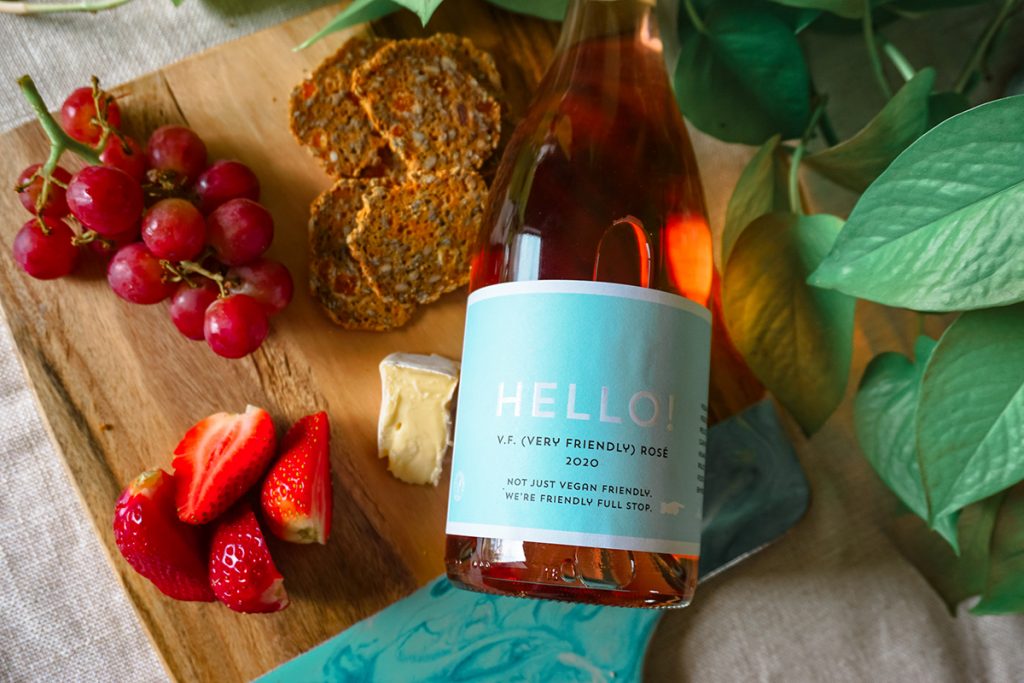 Image of a Hello! Rosé wine bottle against a wooden serving board surrounded by delicious crackers, fresh fruit and cheese. Image supplied