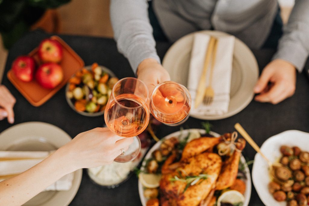 Glasses meet over Christmas dinner. Image by Karoline Grabowska via Pexels.