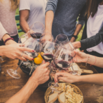 Friends enjoying wine at a wooden farm table. Photographed by Oneinchpunch.