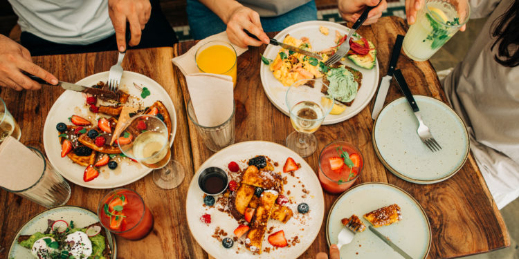 Group of friends eating breakfast or brunch in restaurant. Photographed by Cavan Images. Image sourced via Shutterstock.