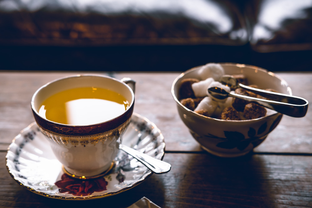 Tea accompanied with a bowl of a sugar cubes. Photographed by John Tecuceanu. Image via Unsplash