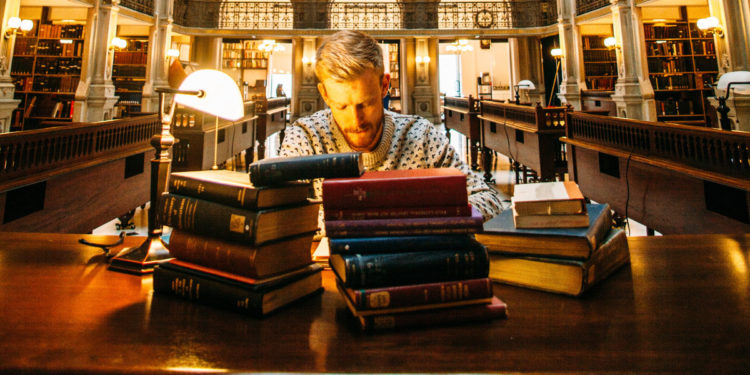 Man reading books. Photographed by Elijah Hail. Image via Unsplash