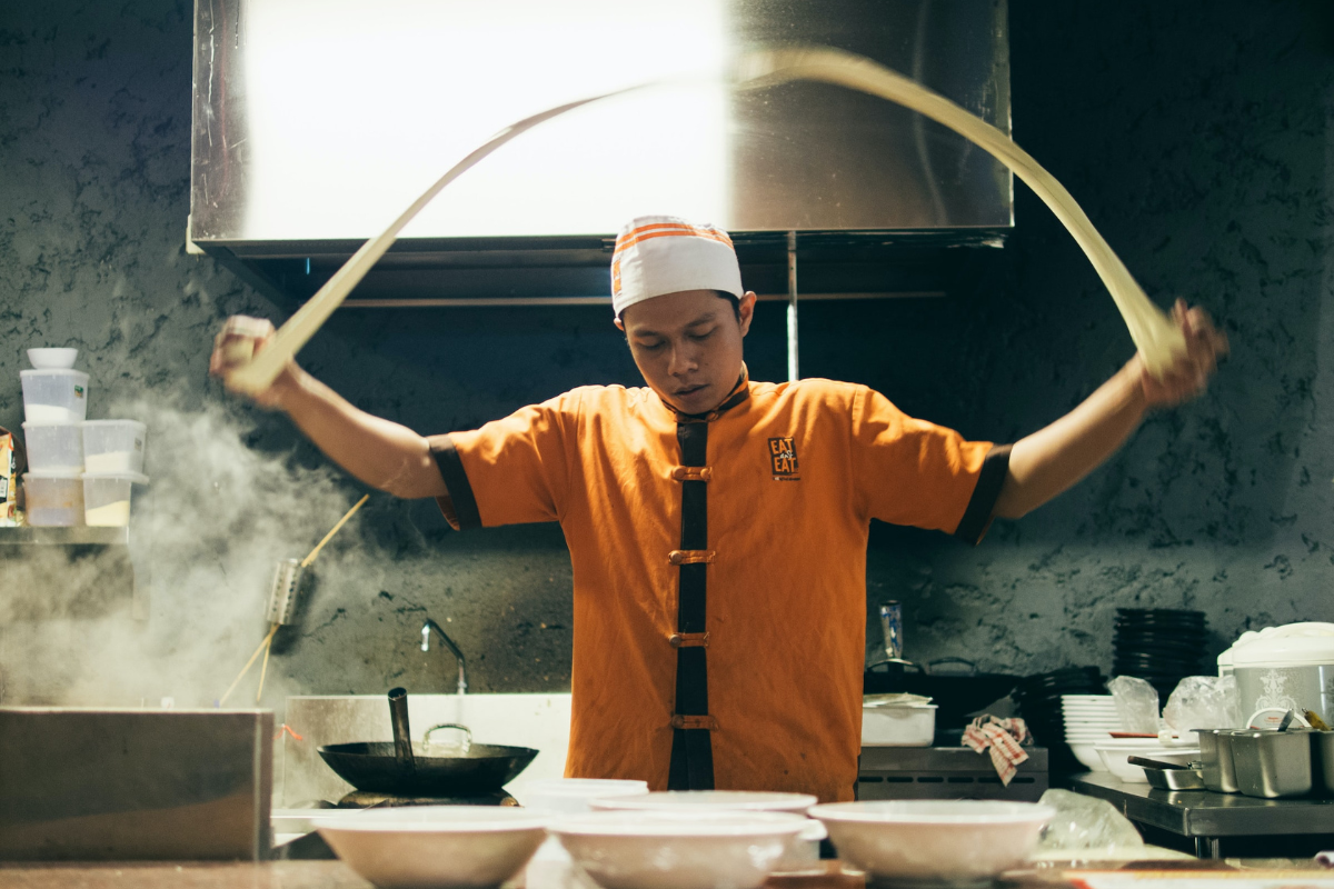 Man stretching dough. Photography by Aditya Romansa. Image via Unsplash