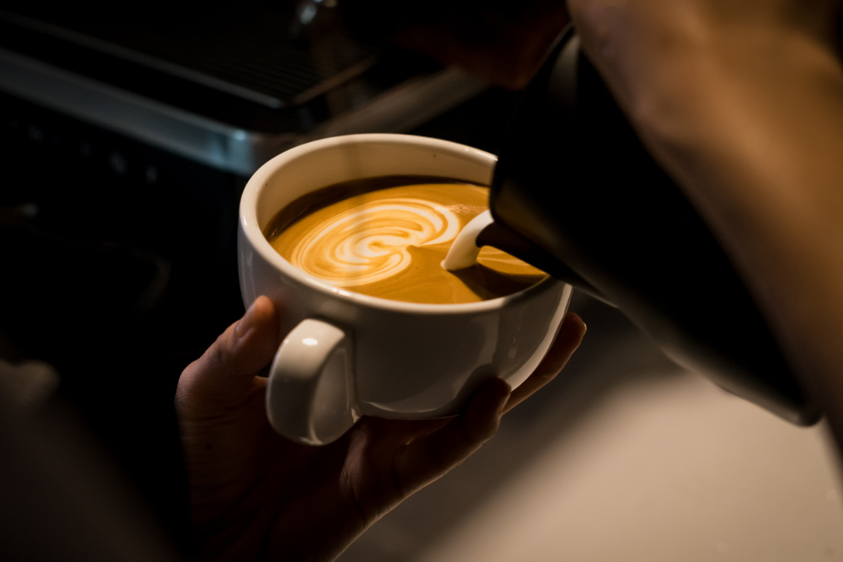 Barista pouring into mug. Photography by Jayden Sim. Image via Unsplash