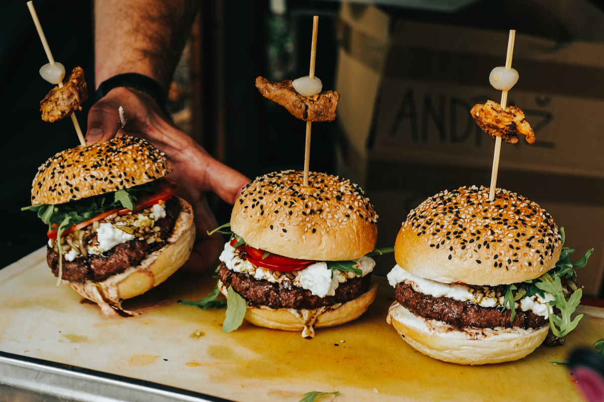 Three burgers on table. Photography by Miha Rekar. Image via Unsplash