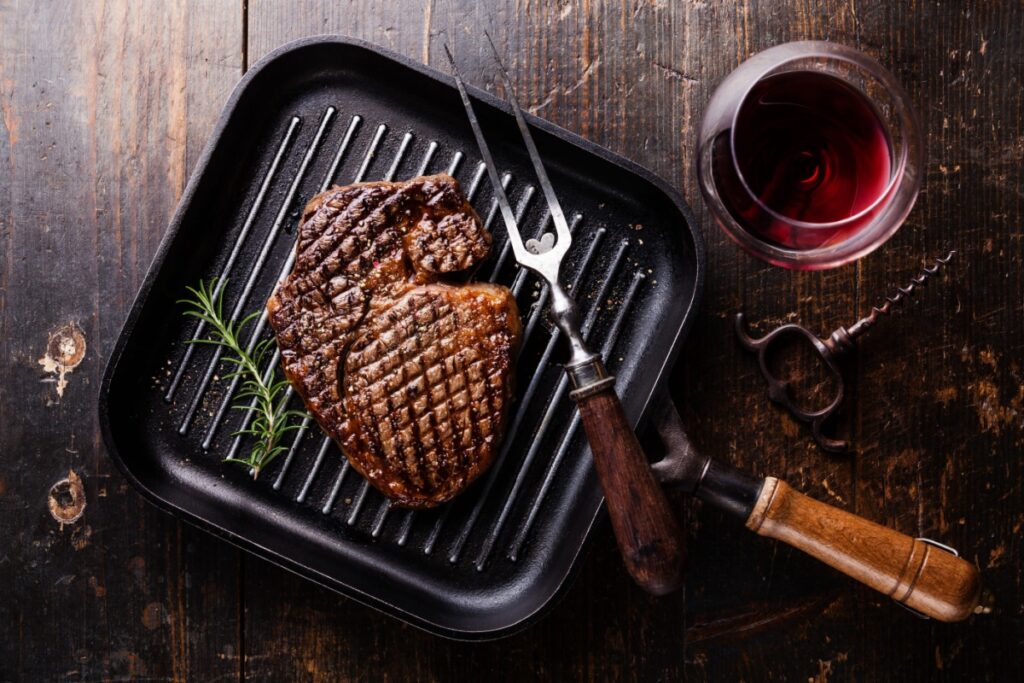 Grilled Black Angus Steak Ribeye on grill iron pan on wooden background with wine. Photography by Natalia Lisovskaya via Shutterstock